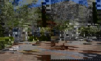 A quaint house on the side of the mountain, with a tiled garden that has an olive tree and a fountain